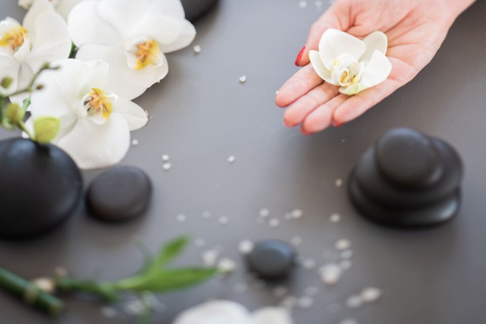 Hands holding a white orchid over hot stones, a spa gift at Jiameng Huntington