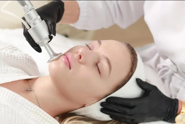 Esthetician in gloves performing an RF lifting and firming facial with a handheld device in Huntington NY