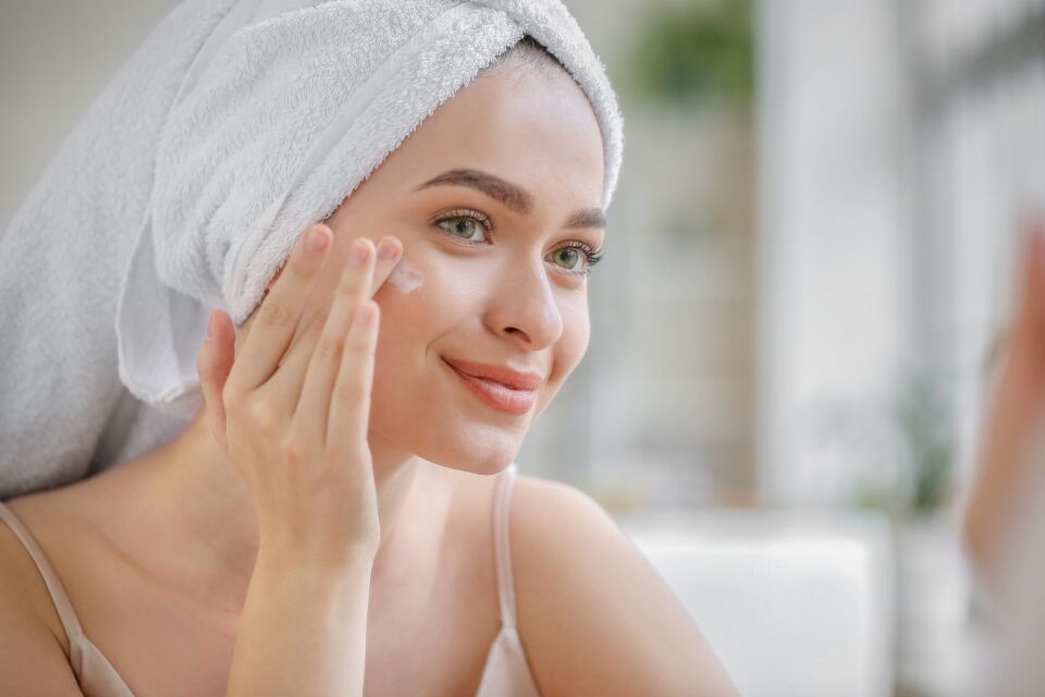 Guest in a towel wrap applying moisturiser after a facial in Huntington NY
